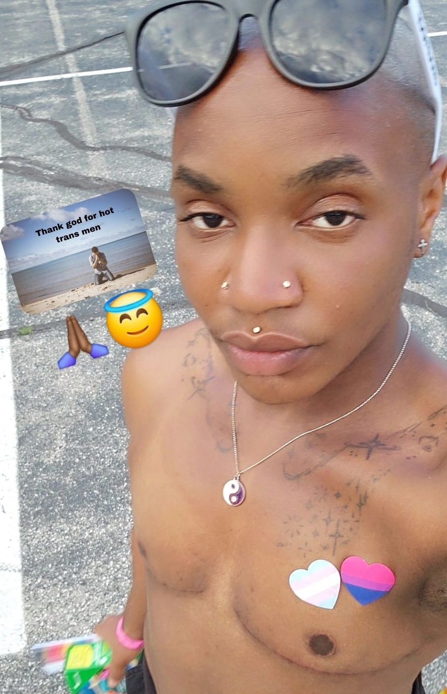 A selfie of Devon Rose, a Black trans non-binary person, wearing trans pride love heart stickers on their chest. There is an image placed in the corner of the picture that says 'Thank god for hot trans men'.