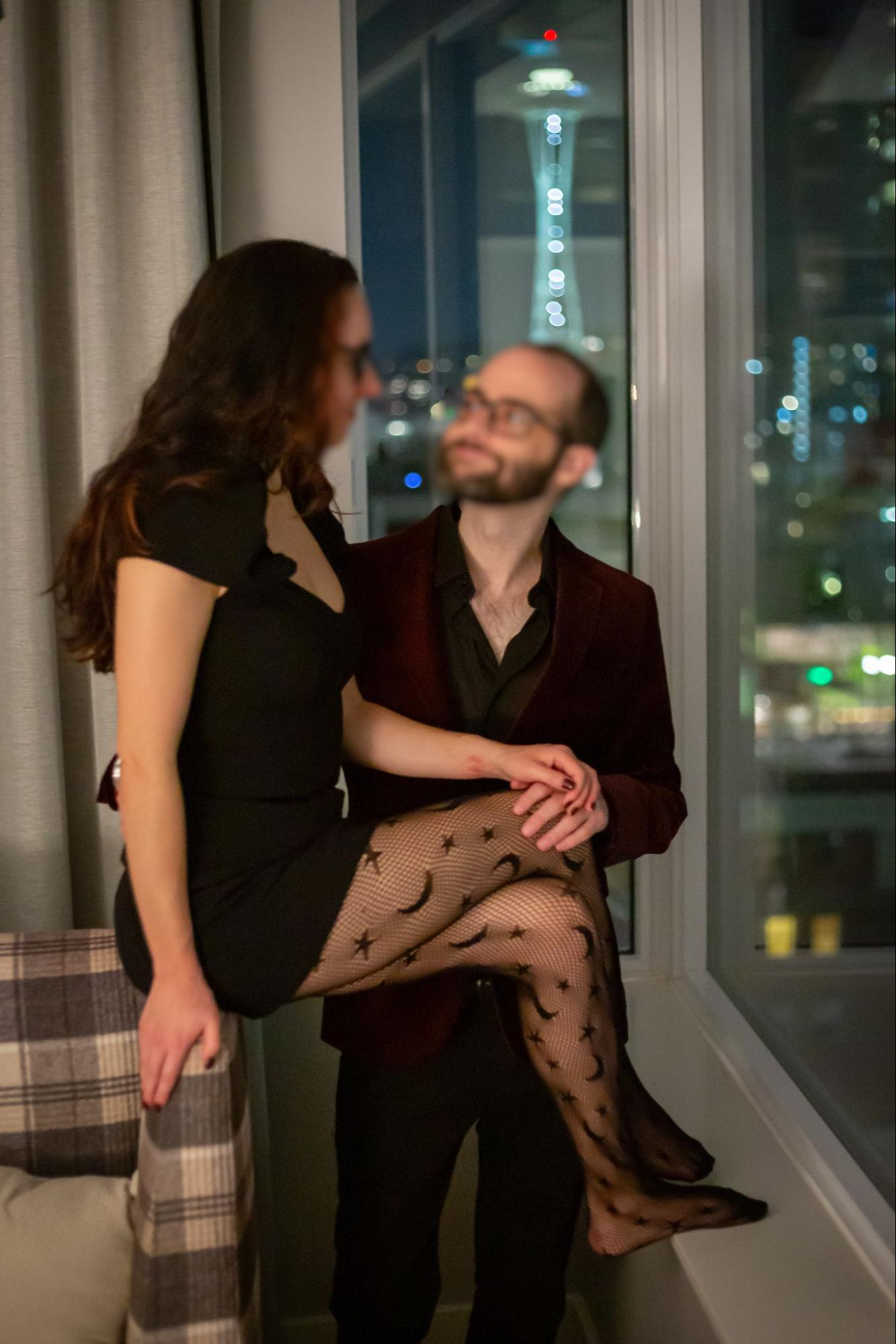 Escorts Maya and Ash near a window at night. Seattle's Space Needle is lit up in the background.