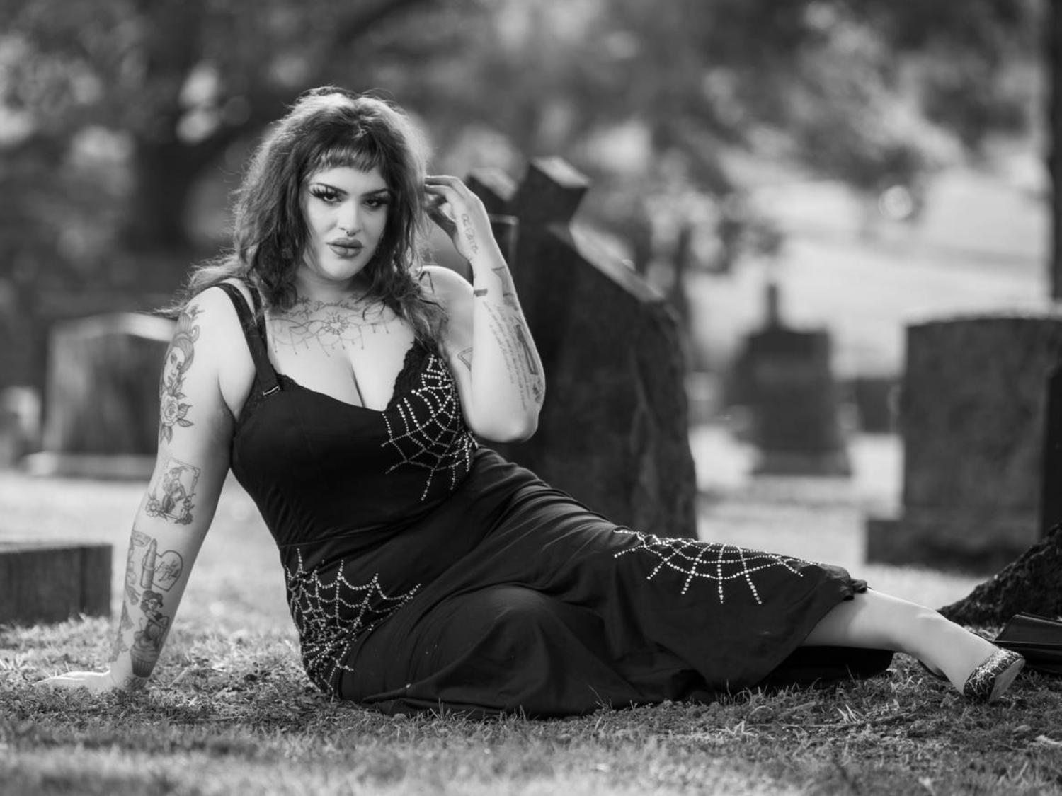 A black and white image of Mistress Ritual posing in a graveyard, wearing a dark-coloured dress with spiderwebs.